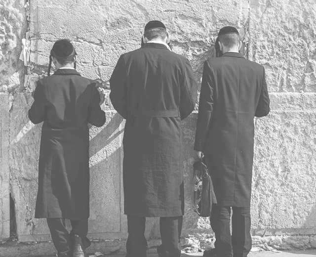 Drei Männer jüdischen Glaubens betend vor der Klagemauer.