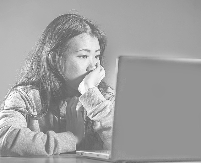 Frau sitzt vor ihrem Laptop und stützt ihr Kinn mit der Hand. 