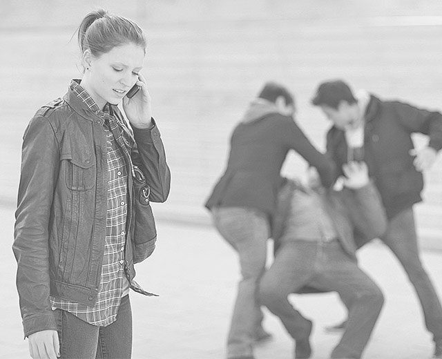 Frau telefoniert im Vordergrund. Im Hintergrund verprügeln zwei Jugendliche einen Mann, der auf dem Boden liegt.